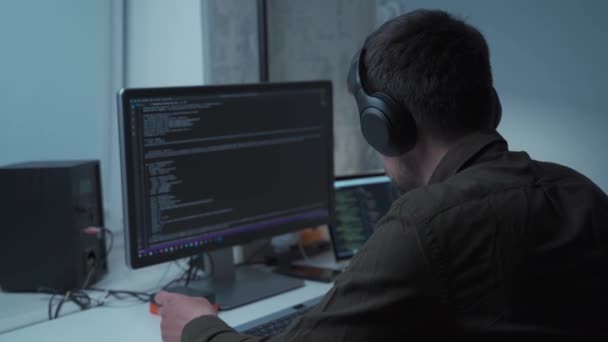 Jóképű férfi szoftverfejlesztő programozási kódok, miközben a laptop mögött dolgozik fejhallgatóval otthonról. Informatikai mérnök a fülhallgatóban, számítógépen dolgozik az irodában. Szabadúszó munkák, társadalmi távolság — Stock videók