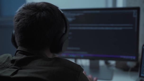 Evden gelen kulaklıklarla dizüstü bilgisayarın arkasında çalışırken yakışıklı erkek yazılım geliştirici kodları. Ofiste bilgisayar üzerinde çalışan kulaklık mühendisi. Serbest Çalışan, Sosyal Mesafe — Stok video