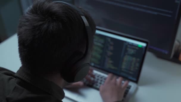 Schöne männliche Softwareentwickler programmieren Codes, während sie von zu Hause aus hinter Laptop mit Kopfhörern arbeiten. IT-Ingenieur mit Kopfhörer am Computer im Büro. Freiberufler arbeitet, soziale Distanzierung — Stockvideo
