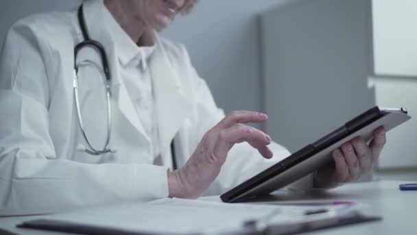 Medelålders kaukasiska kvinnliga läkare i glasögon och medicinsk klänning arbetar med digital tablett och studerar information om läkemedel för konsultation patient på kliniken kontor. Medicin och hälsovård — Stockvideo