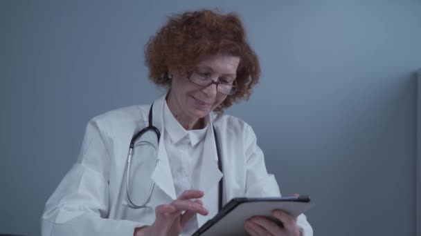 Senior vrouwelijke professionele arts die werkt met digitale tablet telegeneeskunde toepassing in het ziekenhuis kantoor werken online. Gezondheidstechnologie e-health concept. Coronavirus, COVID-19 — Stockvideo