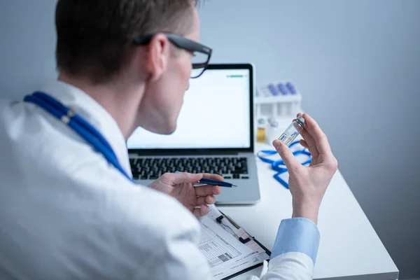 Scientist in medical laboratory examines vial of medicine, vaccine against viruses, influenza, covid. Doctor enters information into computer about investigation. Immunization from terrible diseases — Stock Photo, Image