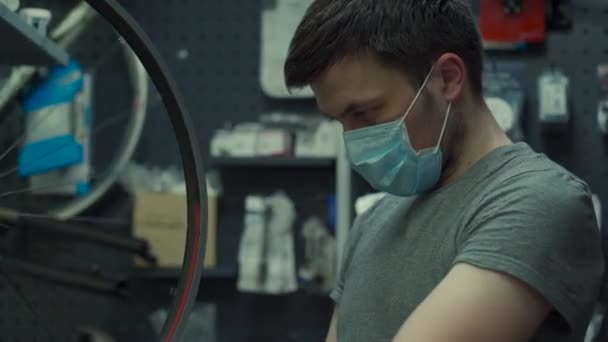 Bicycle mechanic wearing protective mask and gloves repairs customers bicycle wheel in accordance with quarantine standards during coronavirus pandemic. Small business during covid 19 lockdown — Stock Video