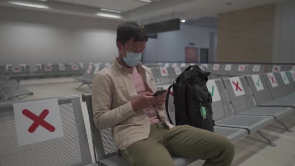 En attente d'un vol à l'aéroport vide de Chypre. Homme assis sur une chaise avec marqueur de distance sociale au terminal vide de Paphos. Vols annulés pendant la quarantaine. Effondrement des compagnies aériennes au coronavirus — Video