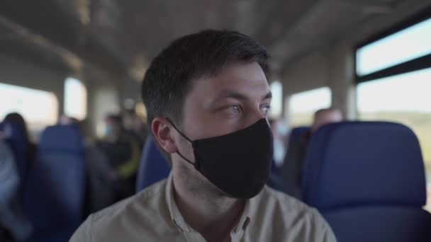 Mann, der mit dem Zug unterwegs ist und eine Gesichtsmaske trägt. Soziale Distanzierung bei Bahnreisen während der Covid-19-Pandemie. Männliche Pendler, die in öffentlichen Verkehrsmitteln zur Arbeit fahren, tragen Mundschutz. Neues Normkonzept — Stockvideo