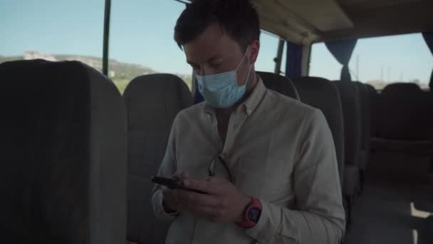 Een mannelijke passagier met een beschermend masker zit op een lege kleine bus tijdens zijn reis in Paphos, Cyprus. Man die pendelt met een oude bus tijdens een coronavirus pandemie. Sociale afstand. Geen masker, geen ingang. Nieuwe norm — Stockvideo