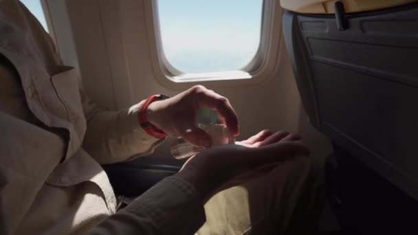 Handgehaltene Aufnahmen zeigen einen Mann mit Gesichtsschutz, der an Bord eines Flugzeugs Desinfektionsmittel einsetzt. Mann mit Schutzmaske benutzt Alkohol-Gel, desinfiziert Hände im Flugzeug, Covid-19-Schutz, neues normales Reisekonzept — Stockvideo
