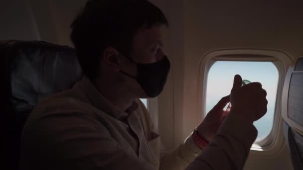 O homem na máscara desinfecta mãos aplicam o desinfetante de álcool, a bordo do avião. Novo normal, segurança e viagens durante o COVID-19. Viajando durante a epidemia de coronavírus. Passageiro aplica antisséptico — Vídeo de Stock