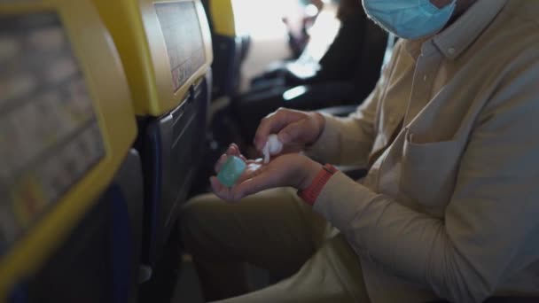 Man on airplane, plane disinfects hands apply gel with disinfection alcohol for hands against Covid-19 pandemic, health prevention. Flight during coronavirus, passenger uses an antiseptic on board — Stock Video