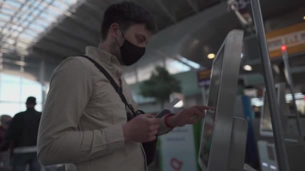 Человек в защитной маске в киоске саморегистрации в аэропорту. Мужчины пользуются автоматом регистрации в аэропорту, чтобы получить посадочный талон. Социальная дистанция, самостоятельная регистрация багажа в терминале во время карантинного шабаша 19 — стоковое видео