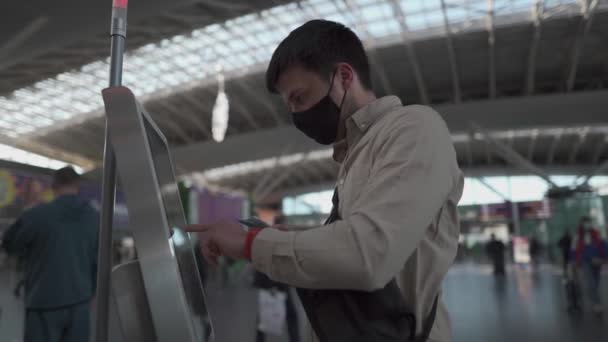 マスクセルフチェックイン手荷物の旅客機内での端末での飛行、旅行の安全コンセプト、新しい通常、コロナウイルス発生中の社会的距離。男は空港でセルフサービスのチェックを使用します — ストック動画