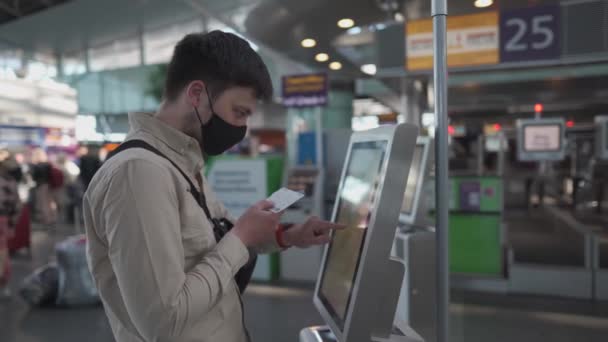 Человек в защитной маске в киоске саморегистрации в аэропорту. Мужчины пользуются автоматом регистрации в аэропорту, чтобы получить посадочный талон. Социальная дистанция, самостоятельная регистрация багажа в терминале во время карантинного шабаша 19 — стоковое видео
