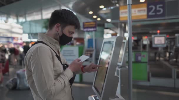 Uomo in maschera protettiva utilizzando self-check-in chiosco in aeroporto. Uso maschile check-in macchina in aeroporto ottenere carta d'imbarco. Distanza sociale, bagaglio self-check-in nel terminal durante la quarantena covid 19 — Video Stock