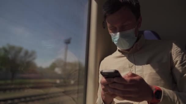 戴面具的人在火车上用手机。一名蒙面男子使用智能手机，在乘坐COVID 19公共交通工具时保持距离。和验尸官一起乘火车旅行新规范 — 图库视频影像