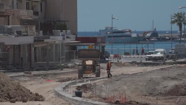 11 de mayo de 2021 Chipre, Paphos. Maquinaria pesada y equipos de construcción están trabajando en la renovación del pavimento cerca del puerto en el centro de Paphos. Concepto de reparación de carreteras. Retroexcavadora en obra — Vídeo de stock