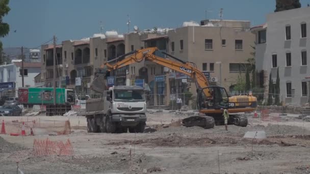 11 Μαΐου 2021 Κύπρος, Πάφος. Κατασκευαστικές εργασίες με κατασκευαστικό εξοπλισμό και εργασίες ανακαίνισης οδών στην πόλη κοντά στο λιμάνι. Κατασκευαστικές εργασίες οδοποιίας με εκσκαφέα, μπουλντόζα και φορτηγό κοντά σε σπίτια — Αρχείο Βίντεο