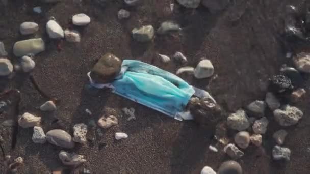 Blauw gebruikte medische masker gegooid op het strand door de zee. Behandeling van voorwerpen en verspilling van medische benodigdheden. Stop de vervuiling van de oceaan. Post covid 19 vervuiling. Afval tijdens het coronavirus. Zeeverontreiniging — Stockvideo