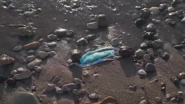蓝色使用医疗面罩扔在海滩上的海路。处理物品和医疗用品的浪费。制止水污染。后系数19污染。在验尸过程中的废物。海洋污染 — 图库视频影像