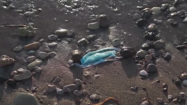 Blauw gebruikte medische masker gegooid op het strand door de zee. Behandeling van voorwerpen en verspilling van medische benodigdheden. Stop de vervuiling van de oceaan. Post covid 19 vervuiling. Afval tijdens het coronavirus. Zeeverontreiniging — Stockvideo