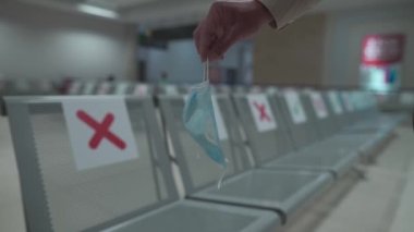 Seyahat konsepti, Coronavirus karantinasında uçuşları yeniden başlatmak. Yeni normal denek. Havaalanı ve yolcuların elindeki sosyal mesafeli sandalyeler tıbbi maske taşıyor. Havaalanında yeni kurallar