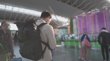 Havaalanında sırt çantalı maskeli gezgin uçuş çizelgesine bakar ve telefon, yeni kural ve uçuş kuralları kullanır. Kontrol alanı elektronik zaman çizelgesinde maskeli sırt çantalı gezgin