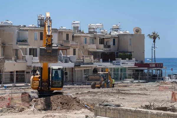 11 Mayıs 2021 Kıbrıs, Paphos. Liman yakınlarındaki inşaat malzemeleri ve yol yenileme işçileri için inşaat işi. Yol inşaatı kazıcı, buldozer ve evlerin yanındaki kamyonla yapılıyor.