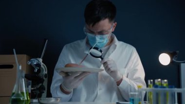 Laboratuvar asistanı elinde büyüteçle çiğ eti inceliyor. Zehir saptaması. Kimya laboratuvarında GDO tavuğunu test eden bir bilim adamı. Adam et örneğine bakıyor ama büyüteç, ürün kalitesi...
