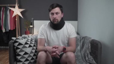 Kazadan sonra köpük yakalı bir adam aniden kanepede boynunda keskin bir ağrı hissetti. Omurga yaralanması. Rahim boynu tasması. Boyun ağrısı olan bir erkek. Baş dönmesi ve servikal kordonu olan özürlü adam evde acı çekiyor.