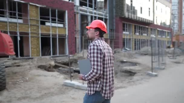 Mladý stavební manažer zkontroluje technickou dokumentaci na staveništi poblíž těžkého traktoru nebo bagru. Kontrolní zpráva Foremana — Stock video