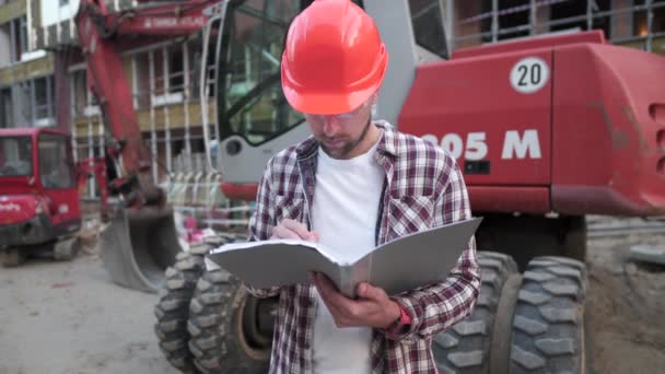 Homem branco engenheiro arquiteto segurando pasta com papéis na escavadeira de fundo, máquinas de construção no local de construção. Construtor olhando para o plano de negócios, documentos arquitetônicos — Vídeo de Stock