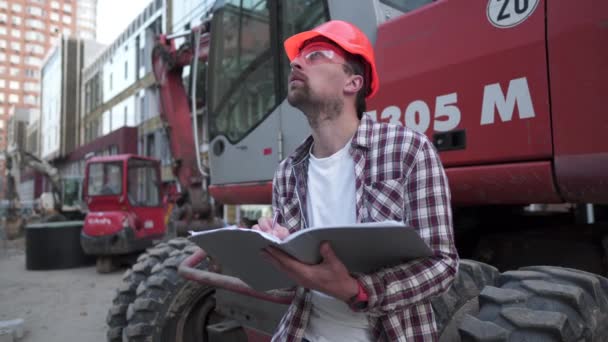 Kavkazský muž inženýr architekt drží složku s papíry na pozadí bagru, stavební stroje na staveništi. Stavitel se dívá na obchodní plán, architektonické dokumenty — Stock video