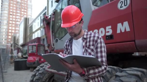 Průmyslový pracovník přezkoumává plány. Stavební dělník držící projektovou dokumentaci poblíž buldozeru na staveništi. Stavební manažer, inženýr prozkoumat stavební dokumentaci — Stock video