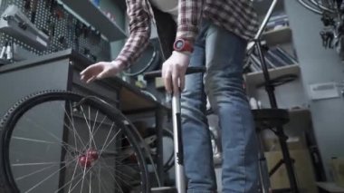 Tamirci bisiklet tekerleğini şişirmek için el pompası kullanıyor. Bisiklet dükkanında tamirci pompa lastiği. Erkek tamirci bisiklet lastiği pompalıyor. Atölyedeki tamir ve servis bisikletleri mühendisi lastik şişirmek için pompa kullanıyor