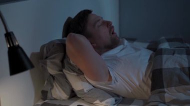 Gece vakti uyuyamayan bir adam. Uyku bozukluğu olan bir erkek. Uykusuzluk çeken bir adam yatakta yatıp tavana bakıyor ve geceleri akıllı telefondan saati kontrol ediyor.