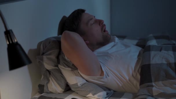 Człowiek nie może zasnąć w nocy. Mężczyzna ma zaburzenia snu. Facet cierpiący na bezsenność leżący w łóżku, patrzący na sufit i sprawdzający czas w nocy na smartfonie. — Wideo stockowe