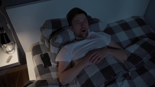 Lonely man cannot sleep in bed at night with eyes wide open, staring at ceiling. Male lying in bed, stressed, worried and cant sleep. Insomnia. Sleepless guy addicted to smartphone instead of sleep — Stock Video