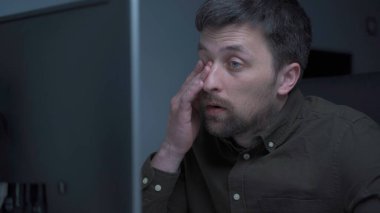 Genç beyaz adam bilgisayar başında fazla mesai yapıyor ve ofisteki monitörden dolayı göz yorgunluğu çekiyor. Erkek, bilgisayar üzerinde çalışırken stresli zaman geçiriyor. Yorgun programcı stresli iş, iş yerinde stres.