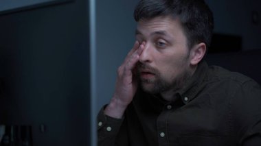 Bilgisayarda çalışan yorgun bir erkek. Ofiste yorgun ve üzgün bir adam. Stresli iş, iş yerinde stres. Yazılım geliştiricisi projenin fazla mesaisi sırasında çok yorgun görünüyor, bilgisayar üzerinde çalışıyor.