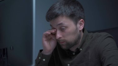 Genç beyaz adam bilgisayar başında fazla mesai yapıyor ve ofisteki monitörden dolayı göz yorgunluğu çekiyor. Erkek, bilgisayar üzerinde çalışırken stresli zaman geçiriyor. Yorgun programcı stresli iş, iş yerinde stres.