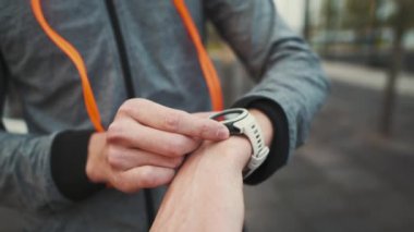 Man checks heart rate on smartwatch after jumping rope workout at street gym. Athlete monitors health, checks pulse on sports watch. Male using fitness watch counts calories burned at jumping rope