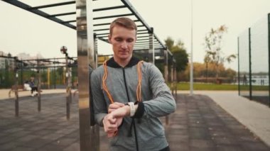 Man measuring pulse on sports watch during training jumping to ropes outdoors. Sporty male with orange rope around his neck setting up smart watch. Records the results of workout exercises on device