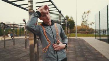 Man checks heart rate on smartwatch after jumping rope workout at street gym. Athlete monitors health, checks pulse on sports watch. Male using fitness watch counts calories burned at jumping rope