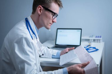 Kalp hastalıklarına zamanında bakmanın konusu. Kalp hastalığı miyokardiyal enfarktüs. Hastane ofisindeki masada elektrokardiyogramı analiz eden doktor. Klinikte kardiyolog. Doktor EKG 'ye bak..