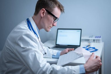 Kardiyolog EKG çıktısı okuyor. Doktor elektrokardiyogramı analiz ediyor. Pratisyen hasta test sonuçlarını inceliyor. Tıbbi ve sağlık hizmetleri konsepti. Hekim muayenehanesinde kardiyograma bakıyor..