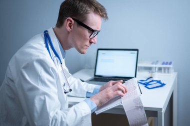 Kardiyolog EKG çıktısı okuyor. Doktor elektrokardiyogramı analiz ediyor. Pratisyen hasta test sonuçlarını inceliyor. Tıbbi ve sağlık hizmetleri konsepti. Hekim muayenehanesinde kardiyograma bakıyor..