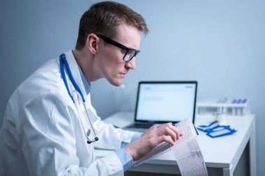 Kalp hastalıklarına zamanında bakmanın konusu. Kalp hastalığı miyokardiyal enfarktüs. Hastane ofisindeki masada elektrokardiyogramı analiz eden doktor. Klinikte kardiyolog. Doktor EKG 'ye bak..