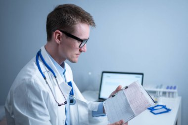 Kardiyolog EKG çıktısı okuyor. Doktor elektrokardiyogramı analiz ediyor. Pratisyen hasta test sonuçlarını inceliyor. Tıbbi ve sağlık hizmetleri konsepti. Hekim muayenehanesinde kardiyograma bakıyor..