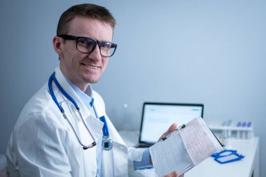 Kalp hastalıklarına zamanında bakmanın konusu. Kalp hastalığı miyokardiyal enfarktüs. Hastane ofisindeki masada elektrokardiyogramı analiz eden doktor. Klinikte kardiyolog. Doktor EKG 'ye bak..