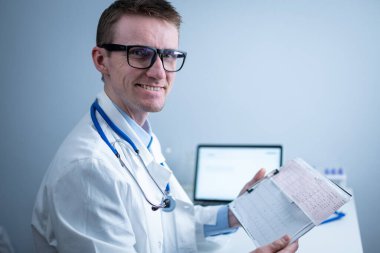 Kalp hastalıklarına zamanında bakmanın konusu. Kalp hastalığı miyokardiyal enfarktüs. Hastane ofisindeki masada elektrokardiyogramı analiz eden doktor. Klinikte kardiyolog. Doktor EKG 'ye bak..