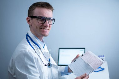 Kardiyolog EKG çıktısı okuyor. Doktor elektrokardiyogramı analiz ediyor. Pratisyen hasta test sonuçlarını inceliyor. Tıbbi ve sağlık hizmetleri konsepti. Hekim muayenehanesinde kardiyograma bakıyor..